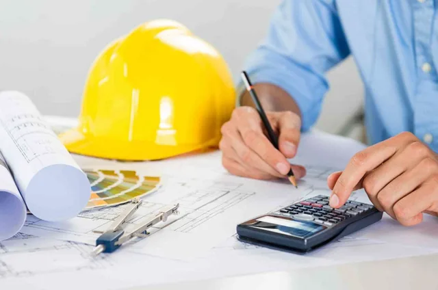 Profissional de engenharia sobre a prancha de projeto, com capacete, calculadora e desenhos técnicos
